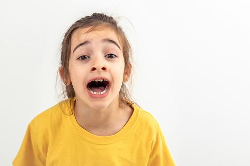 A Caucasian little girl in a yellow T-shirt screams loudly, isolated on a white background, copy space.