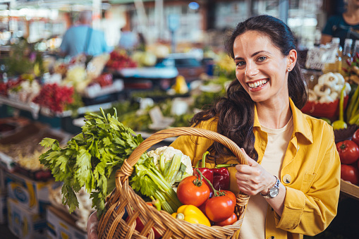 Cheerful woman selecting fresh vegetables in market, everything is fresh and organic. Smiling woman choosing fruits and vegetables on the farmer's market. Woman Buying on Street Market s