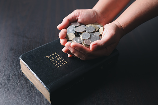 One tenth or tithe is basis on which Bible teaches us to give one tenth of first fruit to God. coins with Holy Bible. Biblical concept of Christian offering, generosity, and giving tithes in church.
