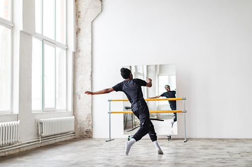 Young black man doing warming up exercises before dancing lesson looking at the mirror