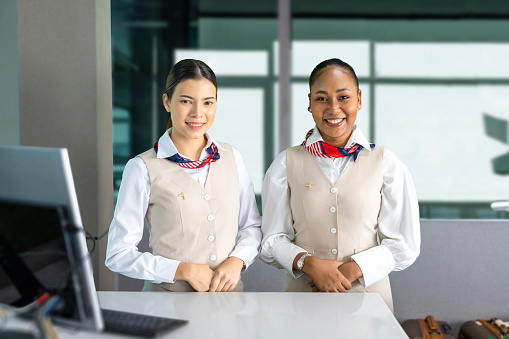 Team of diversity flight attendants posing with smile at the check in counter before boarding aircraft to welcome passenger on board for airline service and airplane transportation concept