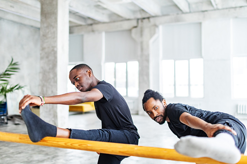Two black male dancer stretching before dance lesson in exercise room