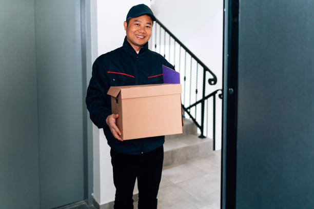 istock Cheerful delivery man standing at the doorstep and delivering a package, while smiling and looking at the camera 1816445322