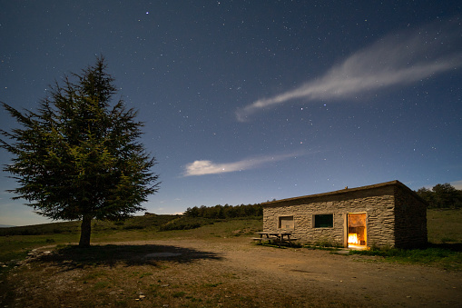 Warm mountain shelter under a starry sky next to a tree