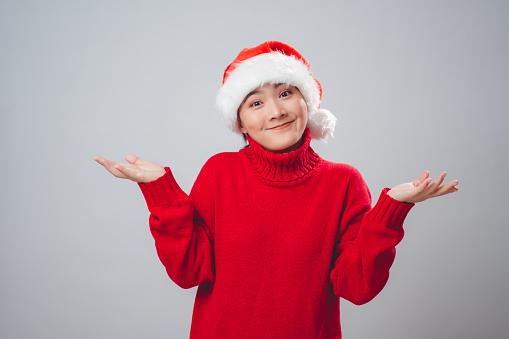 Asian woman wearing Santa hat feel annoyed and shrugging shoulders standing isolated over white background.