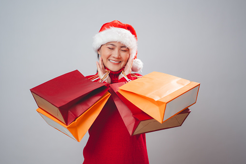 Asian woman wearing Santa hat happy smiling holding shopping bags standing isolated over white background.