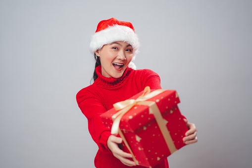 Asian woman wearing Santa hat happy smiling showing gift box standing isolated on white background.