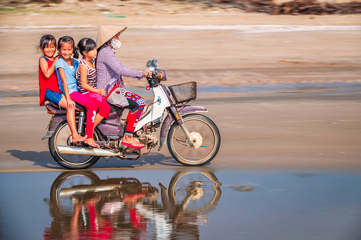 Vietnamese mother with school children riding a motorbike, South Vietnam