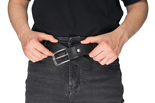 A man in black jeans puts on a belt. Jeans belt. Black leather belt. Buckle.