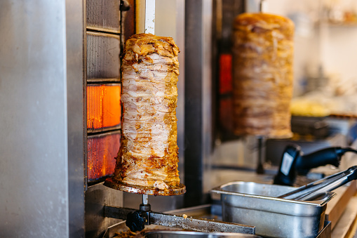 Gyros meat being grilled on a skewer at a fast food kiosk.