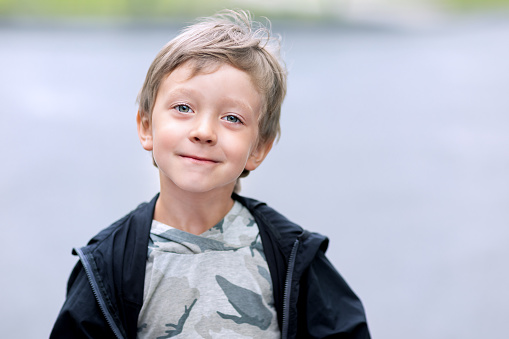 A 6 year old Hispanic boy having fun at the park, standing on playground equipment, smiling and waving at the camera on a sunny spring or summer day.