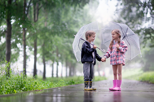 a little boy and a girl are talking outside under umbrellas after the rain