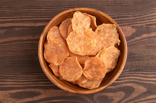 Slices of dehydrated salted meat chips with herbs and spices on brown wooden background. Top view, flat lay, close up.