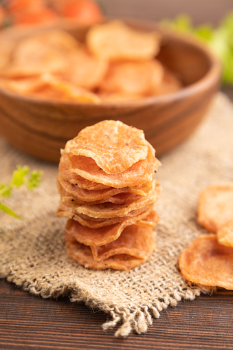 Slices of dehydrated salted meat chips with herbs and spices on brown wooden background and linen textile. Side view, close up, selective focus