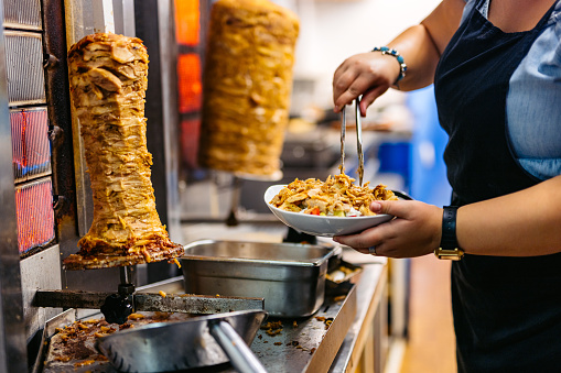 Food service worker preparing fresh salad with gyros meat on a plate at a diner.