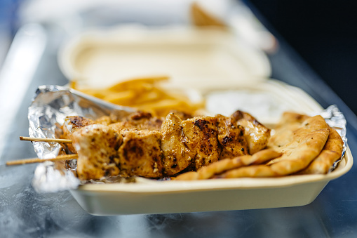 Shish kebab with pita bread, fries and dipping sauce on the side in a take out food container.