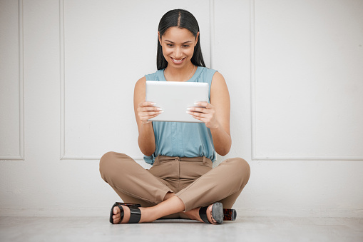 One beautiful mixed race business woman sitting on the floor with her legs crossed and using her digital tablet against a white background. Corporate female worker browsing the internet for research