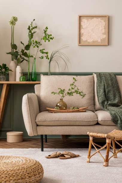 istock Spring composition of living room interior with mock up poster frame, beige sofa, vases with green leaves, stylish pouf, slippers, beige carpet, box and personal accessories. Home decor. Template. 1816533790