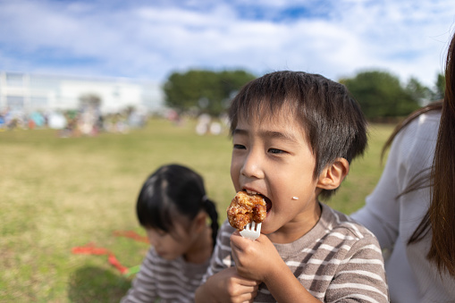 Little boy eating fried chicken in public park