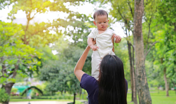 une mère asiatique tenant son bébé dans les bras dans un jardin verdoyant. - enfold photos et images de collection