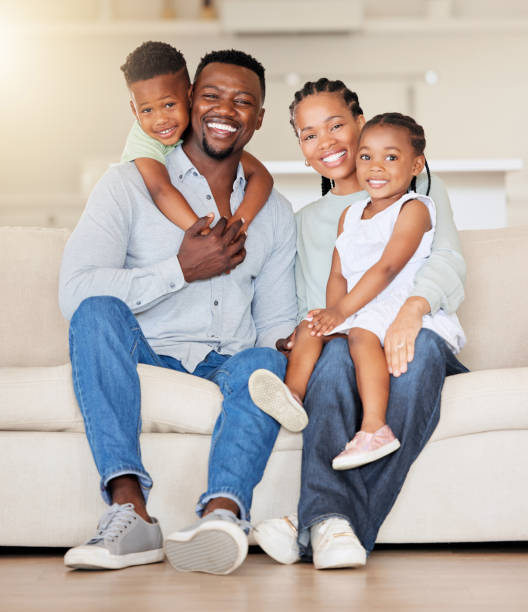 Happy family, portrait or love on couch, care or together for wellness in living room. Black people, woman or man with children for smile face, relax bonding or weekend for gratitude support in house Portrait of a happy african american family with two children sitting on the couch at home. Adorable little girl and boy sitting with their mom and dad. Affectionate family of four bonding at home african ethnicity south africa fitness stock pictures, royalty-free photos & images