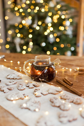 Glass teapot with black tea and gingerbread cookies on a wooden table near Christmas tree
