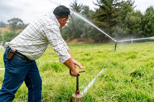 Latin American farmer watering the field with an irrigation system - agriculture concepts