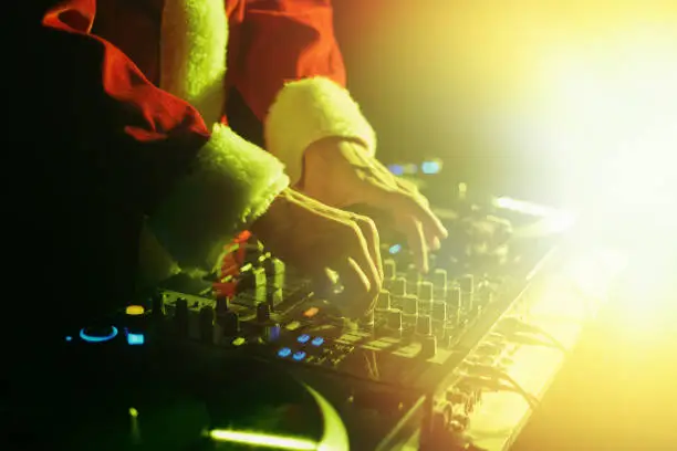 Disc jockey wearing traditional red Santa Claus outfit mixing vinyl records on a Christmas party in night club