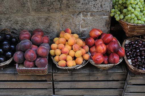 Baskets of fresh peaches, plums, apricots, cherries, grapes and nectarines set on wooden crates in a produce market in Italy.