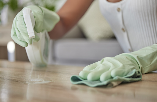 Woman, spray bottle and sanitizer cleaning with a cleaner wiping a table surface with a cloth or rag in the home. Hands, spraying and disinfectant with a female clean bacteria and house work on desk