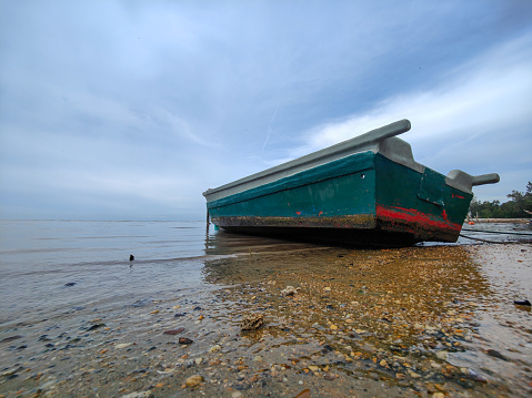 Rubber boat with a motor on gasoline moored to the shore. River bank. Single, empty, grey rowboat/rubber dinghy, with small motor, tied to public pie.