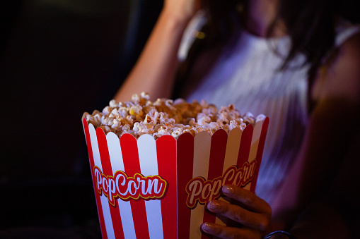 Popcorn in classic striped bukcet on red background. Fluffy maise paper box, copy space. Fast food and movie snack, entertainment concept