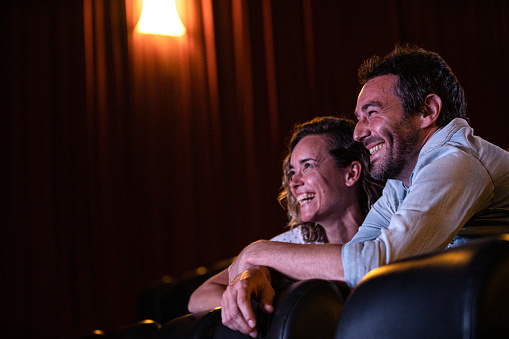 Mid-shot side view of cheerful young couple laughing and having a good time while watching a film inside movie theater