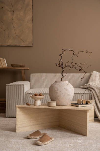 istock Warm and cozy composition of living room interior with travertine coffee table, modular sofa, vase with branch, wooden bench, bowl with nuts, slippers and personal accessories. Home decor. Template. 1816652033
