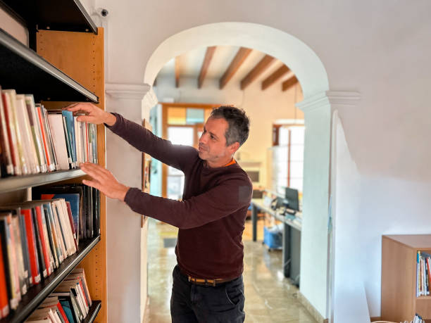 istock Handsome librarian placing books on the shelf in a library 1816659763