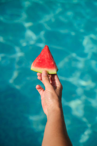 A piece of watermelon in his hand against the background of blue water