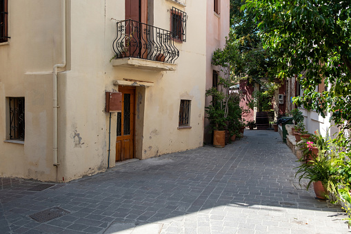 Greece Crete island, Chania Old Town. Pot with plant and flower on narrow empty paved alley, multicolor weathered building, summer sunny day.