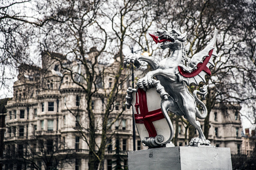 The dragon boundary marks are cast iron statues of dragons (sometimes mistaken for griffins) on metal or stone plinths that mark the boundaries of the City of London. The dragons are painted silver, with details of their wings and tongue picked out in red. The dragon stands on its left rear leg, with the right rear leg lifted forward to support a shield, with the right foreleg raised and the left foreleg holding the top of the shield.