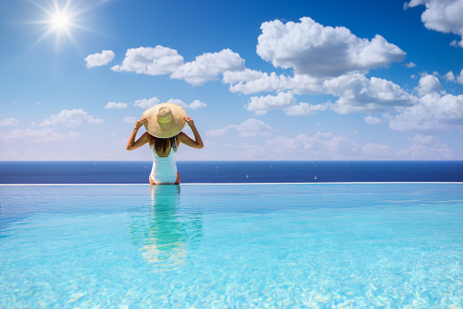 Young caucasian woman in swimming pool on beautiful tropical bay, blue sky and ocean, summer vacation concept.