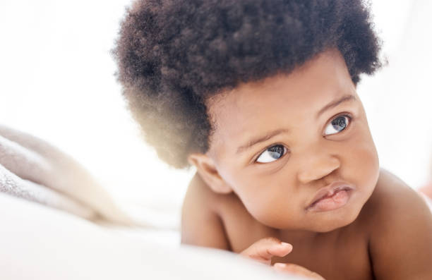 istock Thinking, african and a baby on a bed in the home for growth, curiosity or child development. Face, idea and afro with an adorable little infant in the bedroom of an apartment on a summer morning 1816705533