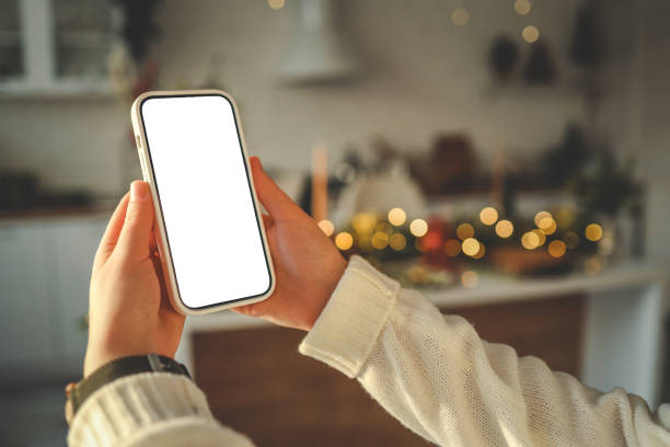 istock Phone in hands with isolated screen on Christmas kitchen background 1816718383