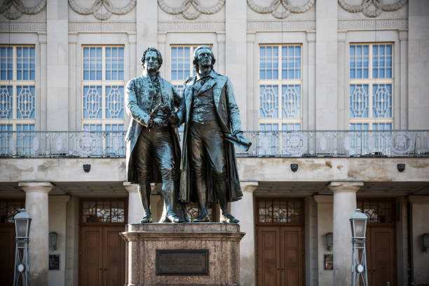 Weimar, Germany - December 23, 2014: The Statues of Goethe and Schiller Located in Weimar.\n\nThe statues of Johann Wolfgang von Goethe and Friedrich Schiller, located in Weimar, Germany, are iconic monuments paying tribute to two of the country's most renowned literary figures. Positioned in front of the German National Theatre in Theaterplatz, the statues symbolize the enduring friendship and intellectual collaboration between Goethe and Schiller, who were pivotal figures in German literature during the Classical and Weimar Classicism periods.\n\nThe statues were unveiled in 1857 and sculpted by Ernst Rietschel. The monument features Goethe and Schiller in animated conversation, embodying the spirit of intellectual exchange and artistic collaboration that defined their relationship. The site has become a symbol of Weimar's cultural heritage, attracting visitors and literature enthusiasts from around the world. It stands as a fitting tribute to the profound impact Goethe and Schiller had on German literature and intellectual thought during a pivotal era in the country's cultural history.