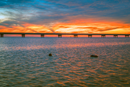 The setting sun casts vibrant light over Pamlico Sound and the Rodanthe Bridge. The bridge is designed to be a sustainable solution to protect against storms. It is located at the northern end of the Pea Island National Wildlife Refuge in North Carolina.