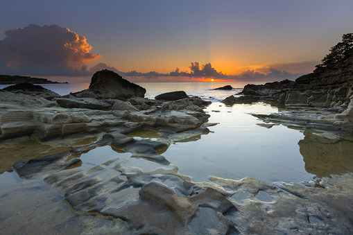 A romantic bay by the sea at sunrise with small lagoons in which the sky is reflected. Lagoons are created by the sea between rounded stones.