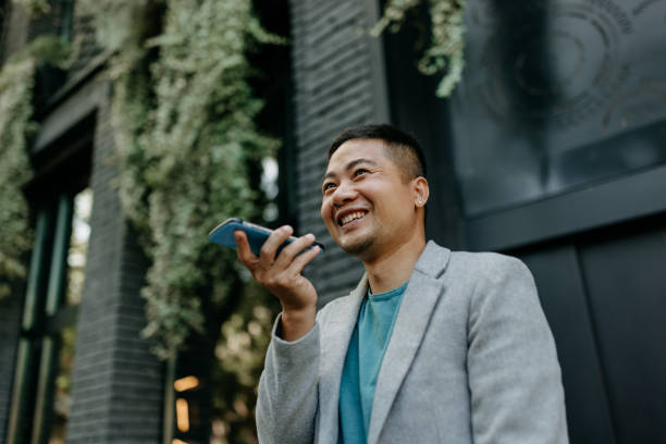I can assist Mid adult Chinese man speaking on the speaker of his phone asian man headphones stock pictures, royalty-free photos & images