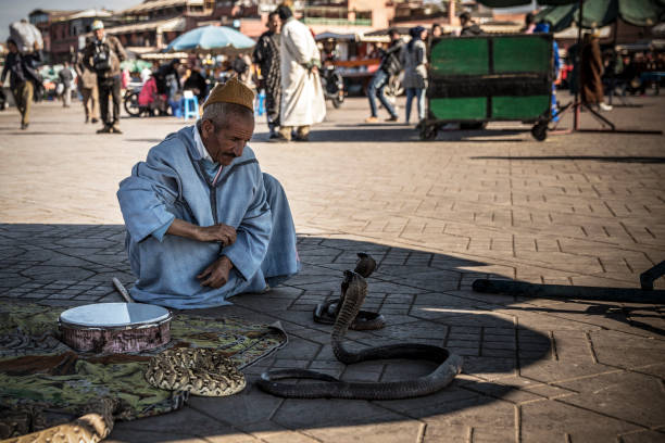 The man in the photo is a Guerrab, a traditional Moroccan water seller commonly seen in Jemaa el-Fnaa, Marrakesh’s famous main square. Dressed in a vibrant red robe and a wide-brimmed, tasselled hat, Guerrabs once roamed cities and deserts offering drinking water from goatskin bags, using brass cups and ringing bells to attract attention. Though no longer needed for water, they are now cultural icons and popular with tourists for photos, preserving a centuries-old tradition that reflects Morocco’s nomadic and market-centered heritage.