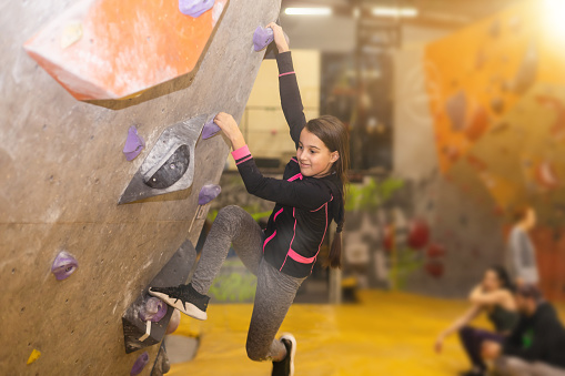 Teenage girl at indoor climbing wall. Kid having fun at bouldering wall. Child learning at climbing class. Sports healthy lifestyle. Youth at climbing summer camp.