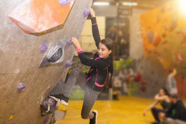 adolescente na parede de escalada interior. garoto se divertindo na parede de pedregulhos. aprendizado infantil na aula de escalada. esporte estilo de vida saudável. jovens no acampamento de verão de escalada - climbing wall rock climbing holding reaching - fotografias e filmes do acervo