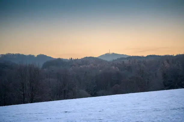 View of Oelberg or Oil mountain in the Siebengebirge or Seven Mountains range near Bonn with its antenna tower visible at sunrise in winter with frosted trees and golden, clear sky