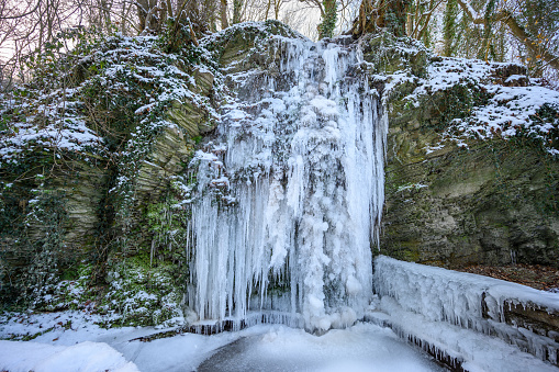 Frozen waterfall or cascade in Unkel, Germany with rocky cliff surrounding it in winter with snow covering the area